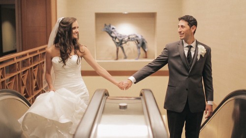 Bride and groom hold hands on escelator