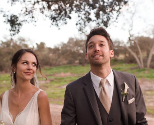 Bride and groom walk under oaks at Mt. Woodson Castle