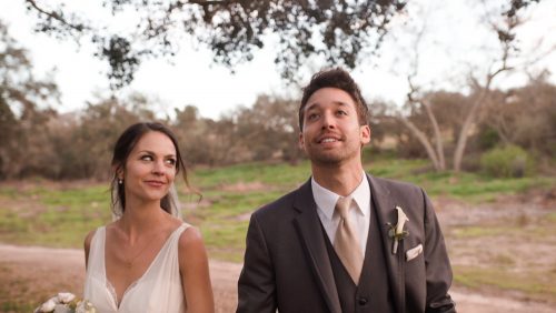 Bride and groom walk under oaks at Mt. Woodson Castle