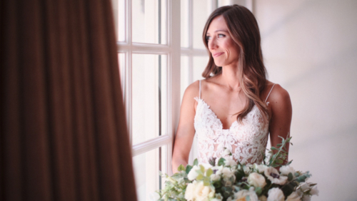bride with bouquet looks out window with beautiful smile