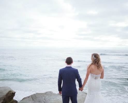 Bride and groom standing on rock in front of ocean