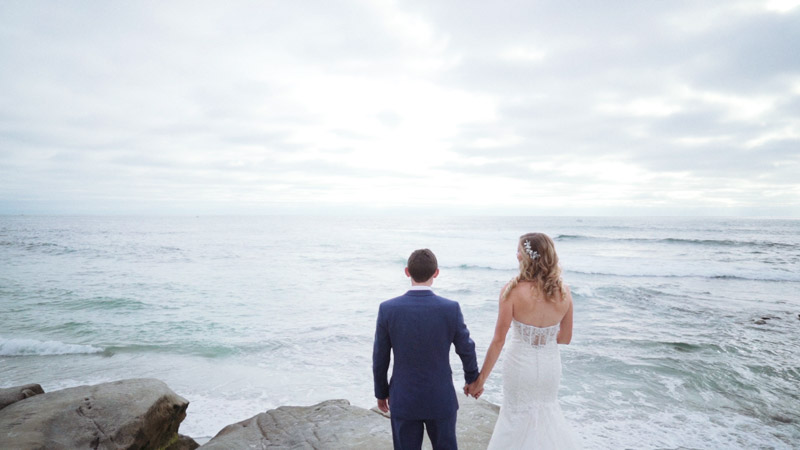 Bride and groom standing on rock in front of ocean
