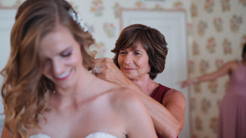 Mom helps bride put on necklace before wedding ceremony
