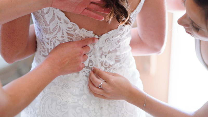 Bridesmaids helps bride lace up wedding dress